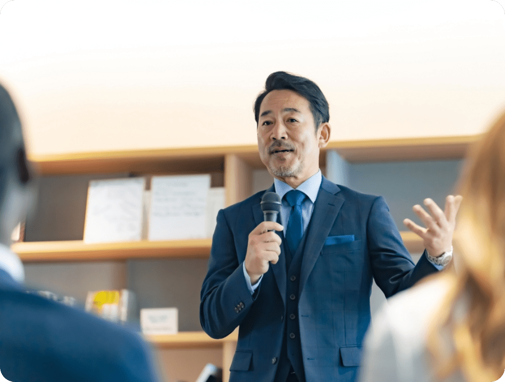 イメージ画像：マイクを持って講演するスーツ姿の男性